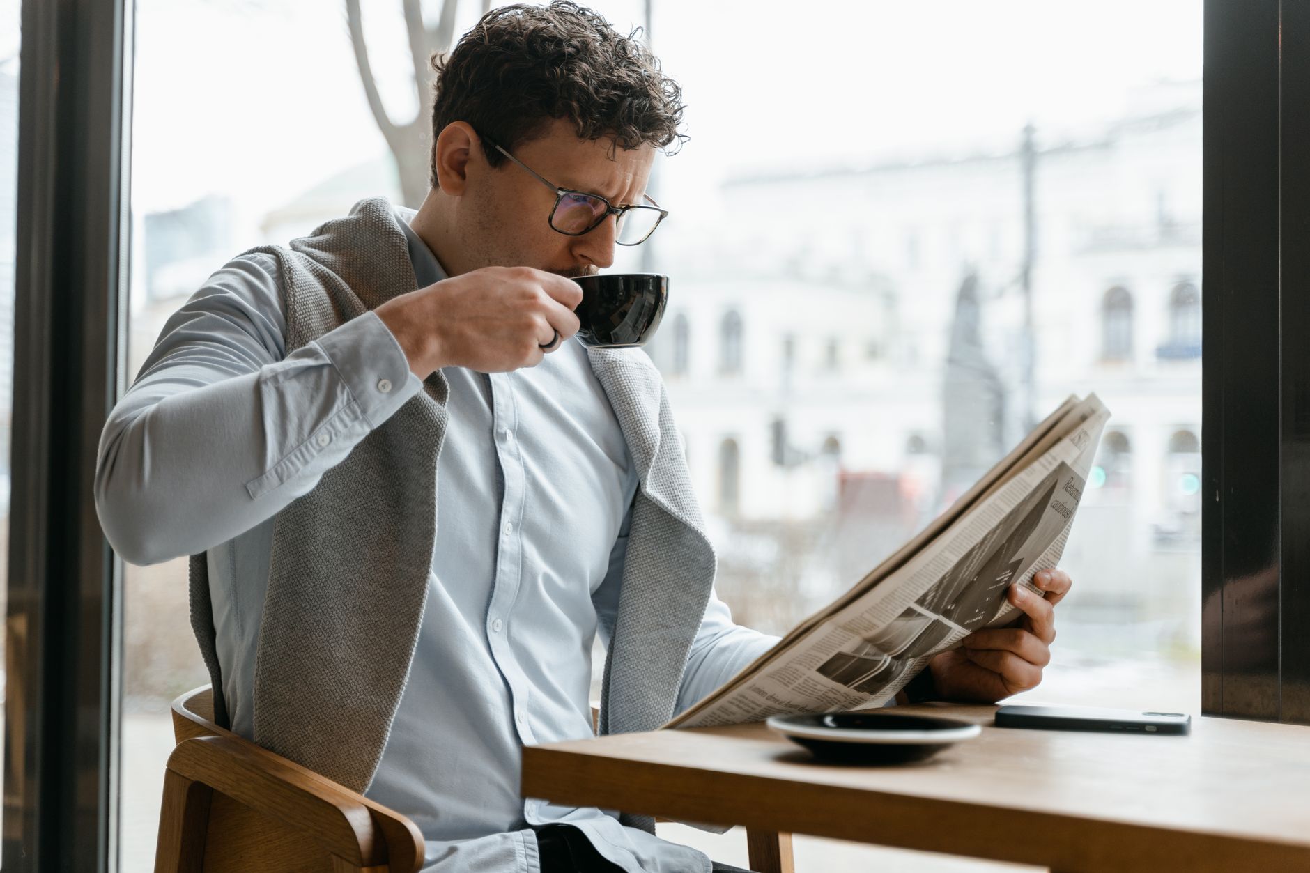 Adult man wearing eyeglasses sipping coffee and reading a newspaper in a cozy cafe setting. — Achtung: Bietet Realz Casino fa
