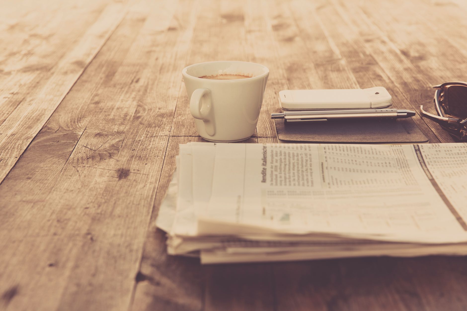 A warm vintage morning setup with coffee, newspaper, and smartphone on wooden table. — test123123